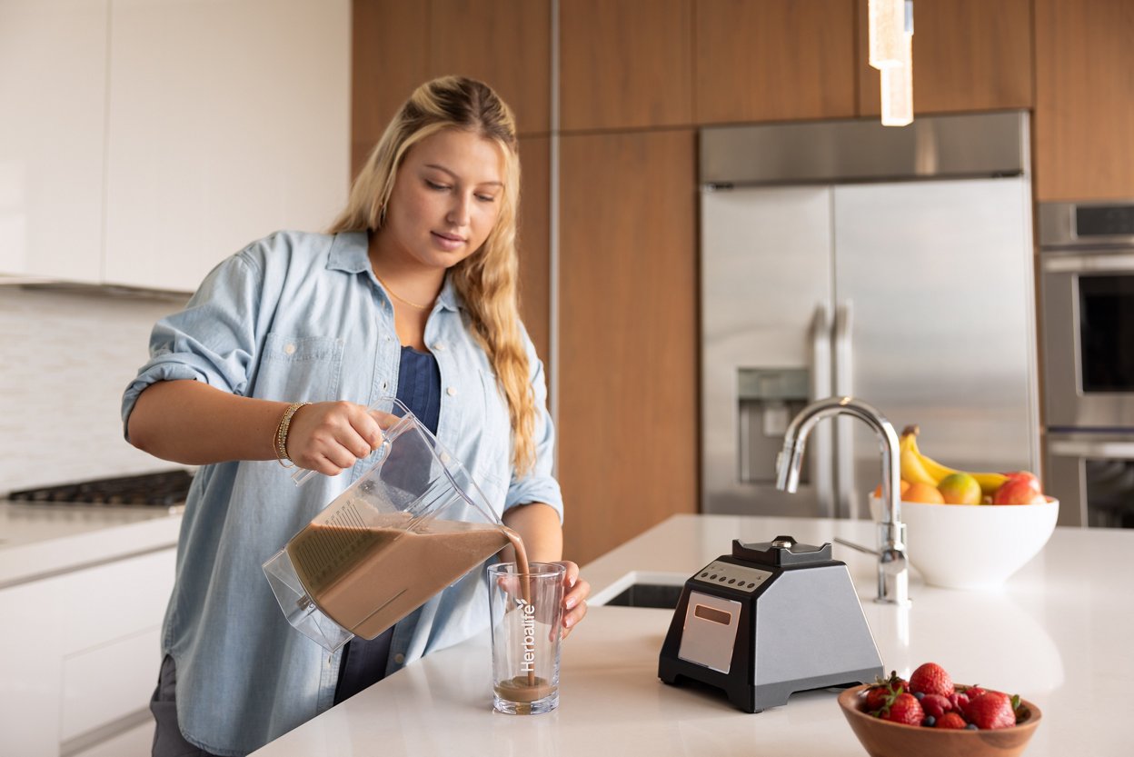 Woman pouring formula 1 shake from the blender at the kitchen